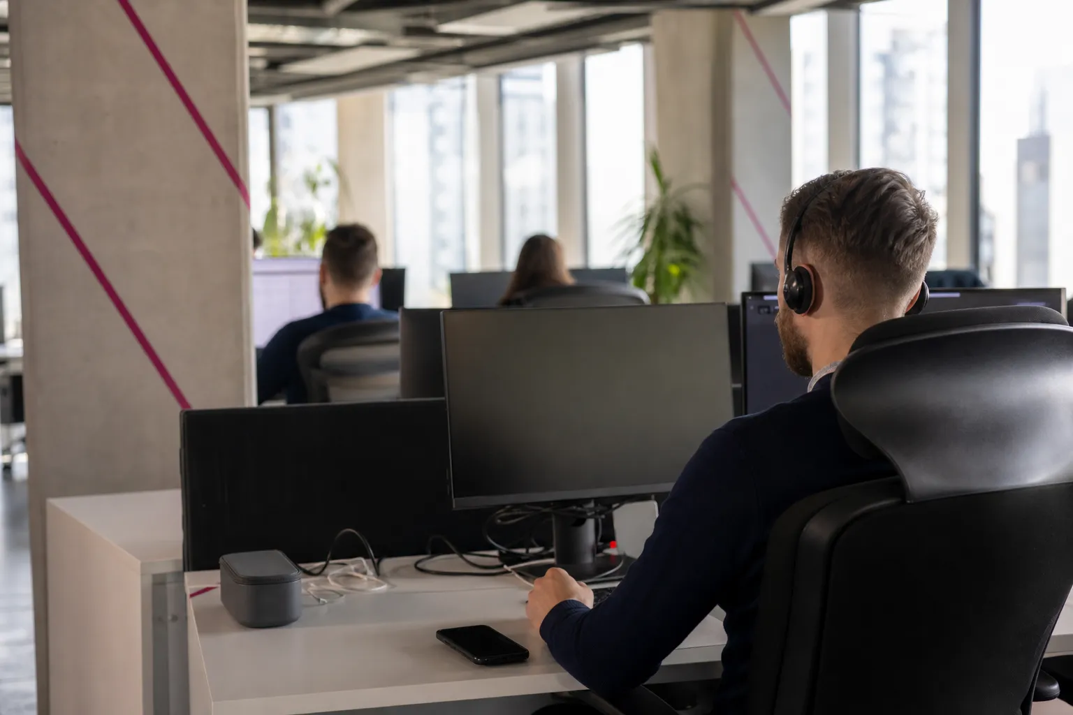 Homme au casque travaillant sur ordinateur en open space moderne, plusieurs écrans et pupitre de coworking. Marché du travail roumanie évoqué.